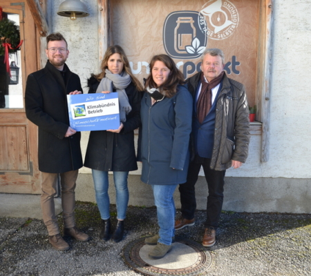Vier Personen stehen mit der Klimabündnis-Tafel vor dem unvperackt-Laden.