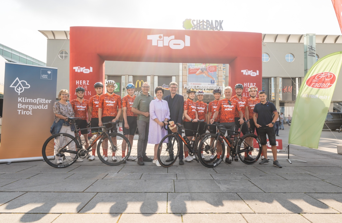 Eine Gruppe von ungefähr 15 Leuten steht in Radkleidung und mit Rädern vor einem Zieleinlauf