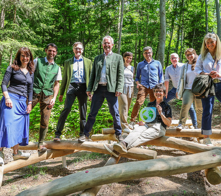 Eine Gruppe an Menschen steht auf Holzstreben im Wald.