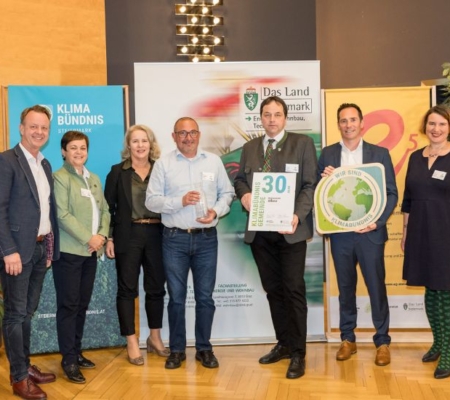 Klimabündnis Auszeichnungsgala: Gemeindevertreter stehen mit Vorständen vor dem Klimabündnis und Land Steiermark Rollup und lächeln. Sie halten die Auszeichnungen in den Händen.