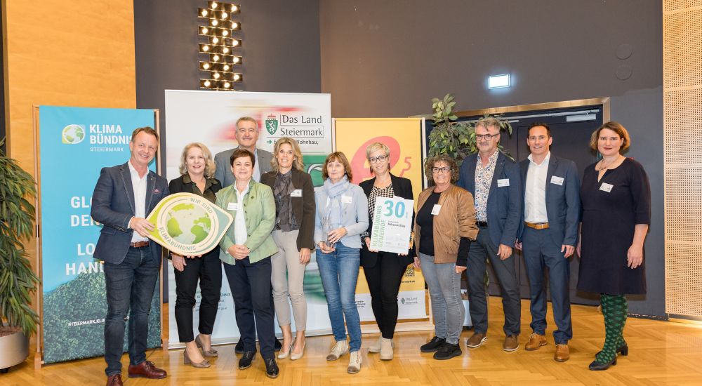 Klimabündnis Auszeichnungsgala: Gemeindevertreter stehen mit Vorständen vor dem Klimabündnis und Land Steiermark Rollup und lächeln. Sie halten die Auszeichnungen in den Händen.