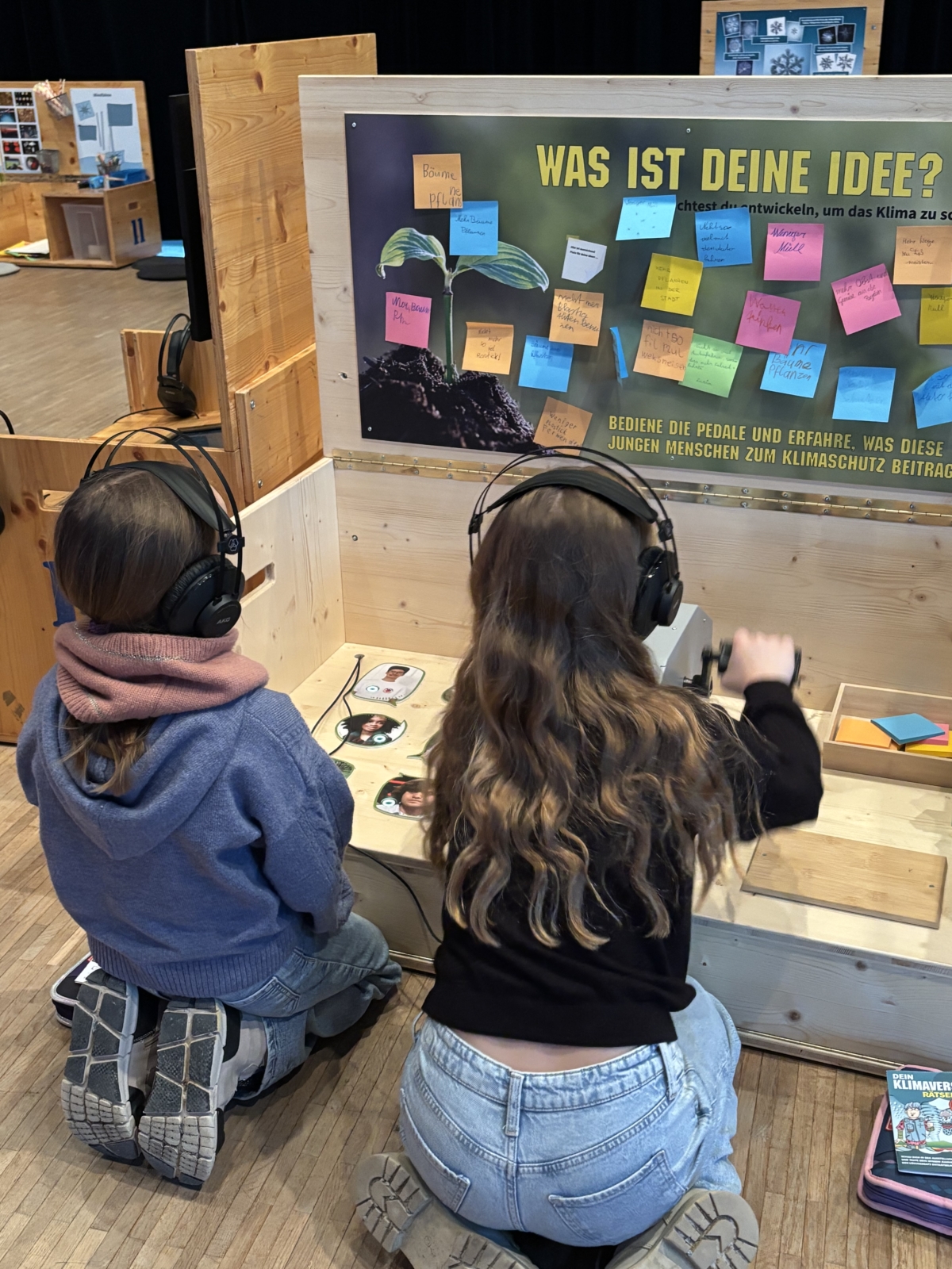 kinder vor holzbox mit handfahrad und hören mit dem kopfhörer die Informationen der Station