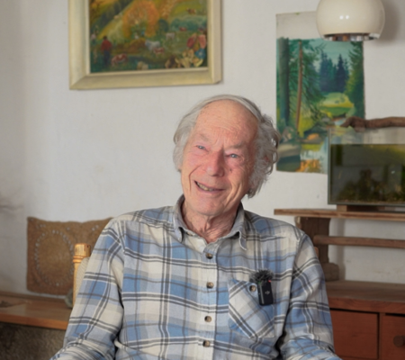 Ein älterer Mann sitzt vor dem Kamin und lächelt in die Kamera