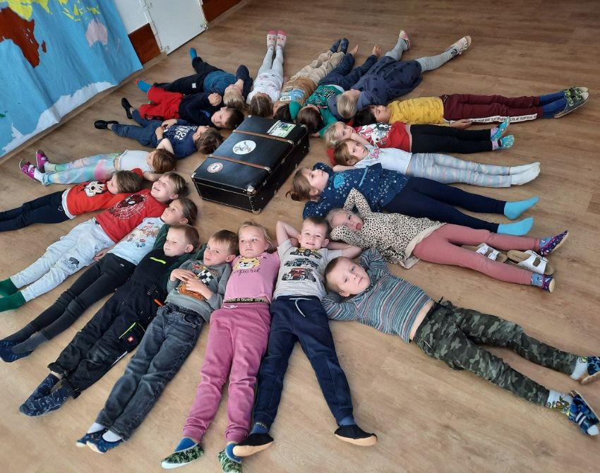 Kinder liegen am Boden im Kreis um einen Koffer