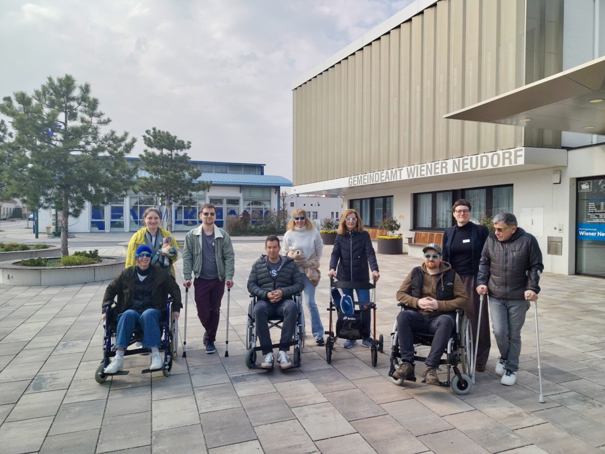 Gruppe von Menschen mit Rollstühlen und Gehhilfen vor dem Gemeindeamt Wiener Neudorf